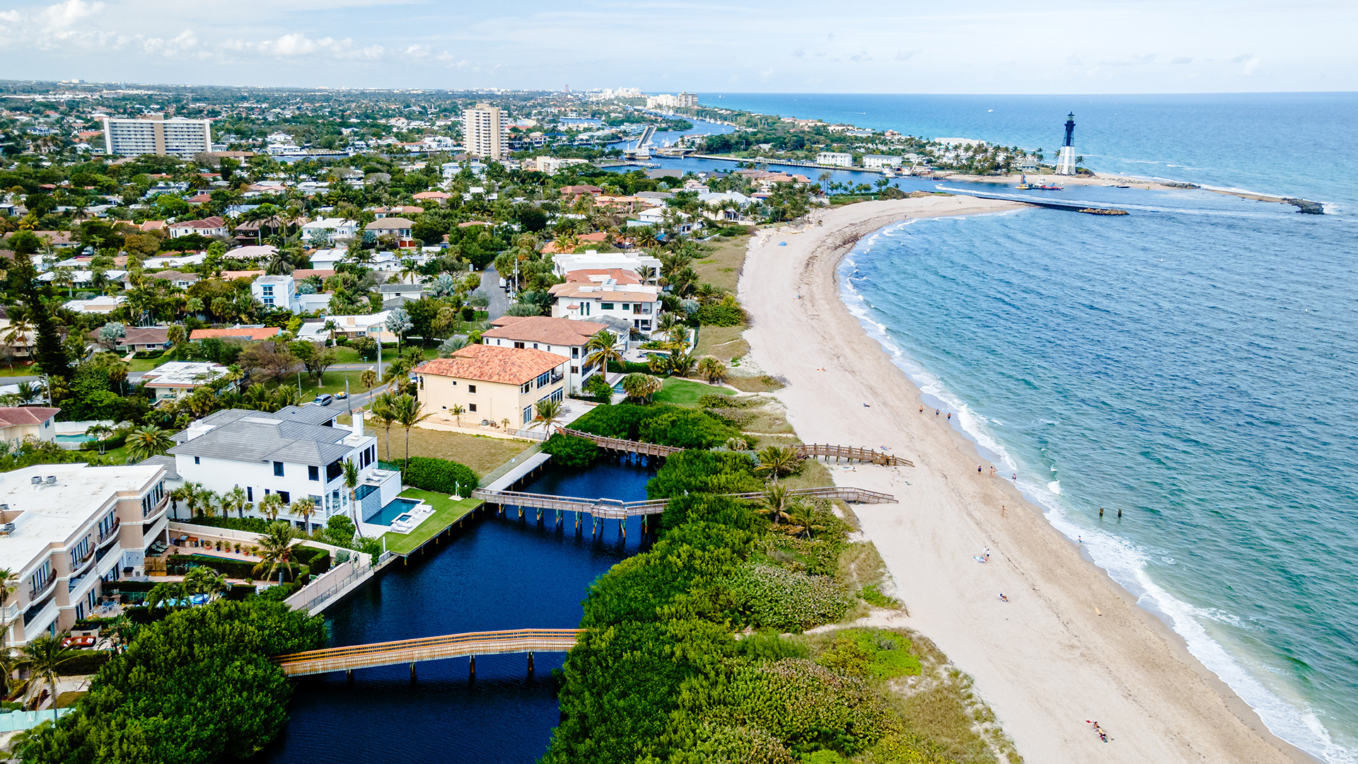 The image shows a coastal cityscape with a beachfront promenade, buildings, and a body of water in the foreground, taken from an elevated perspective.